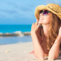 Eine lächelnde Frau mit Hut auf dem Kopf, die am Strand liegt
