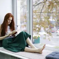 Eine schöne barfüßige Frau sitzt am Fenster und liest