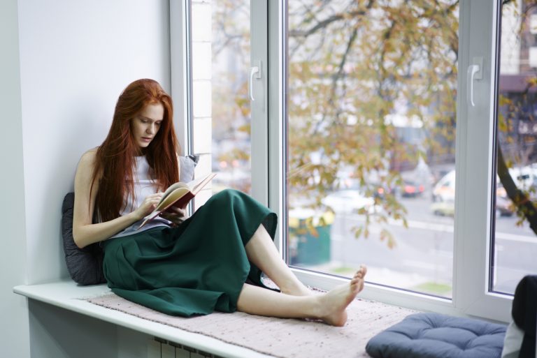 Eine schöne barfüßige Frau sitzt am Fenster und liest