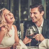 Ein lächelnder Mann und eine lächelnde Frau stoßen mit Wein und Lachen an