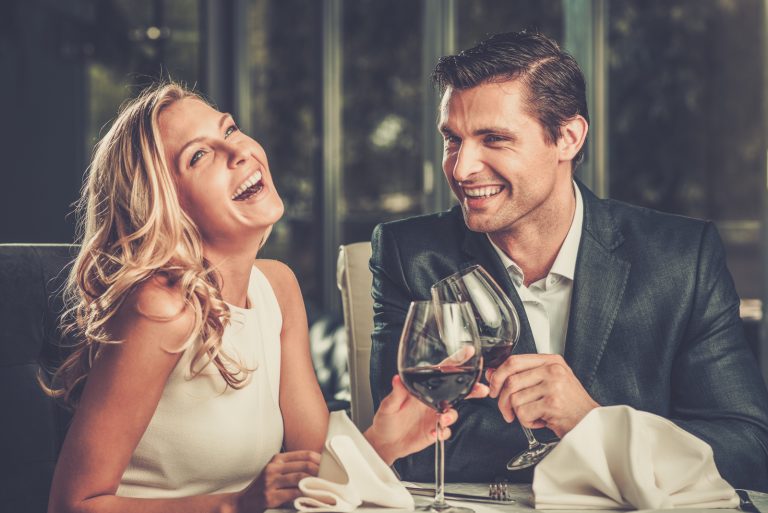 Ein lächelnder Mann und eine lächelnde Frau stoßen mit Wein und Lachen an