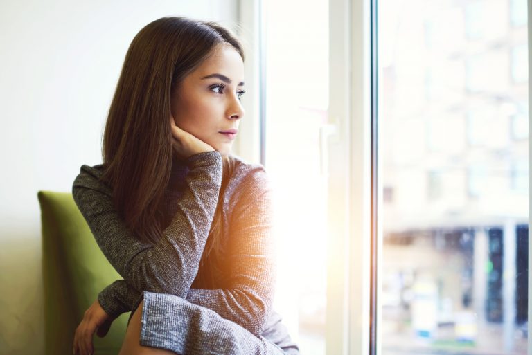 Frau, die im modernen Kaffeeinnenraum nahe riesigem Fenster sitzt