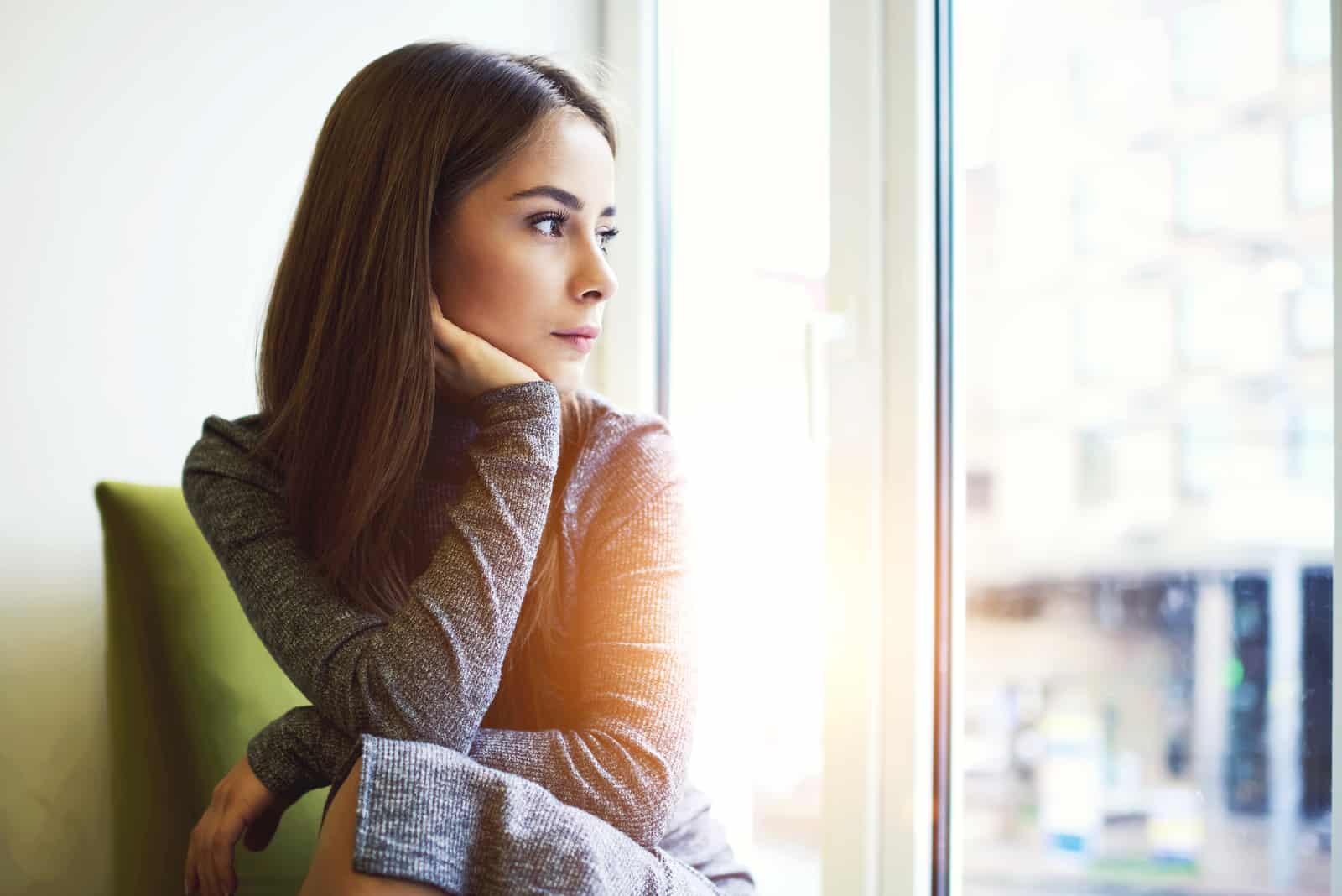 Frau, die im modernen Kaffeeinnenraum nahe riesigem Fenster sitzt