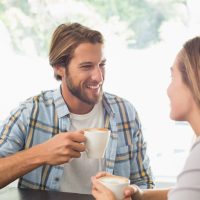 Ein lächelnder Mann und eine lächelnde Frau unterhalten sich beim Kaffee