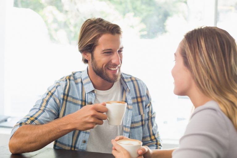 Ein lächelnder Mann und eine lächelnde Frau unterhalten sich beim Kaffee