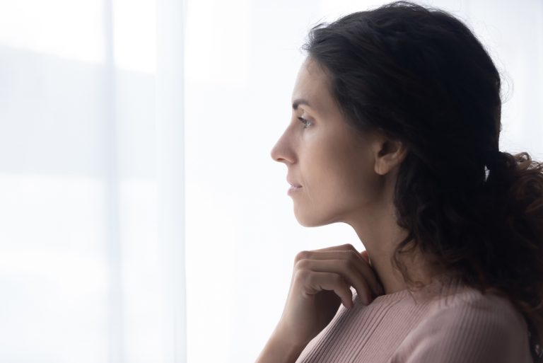 nachdenkliche junge kaukasische frau, die nahe fenster steht