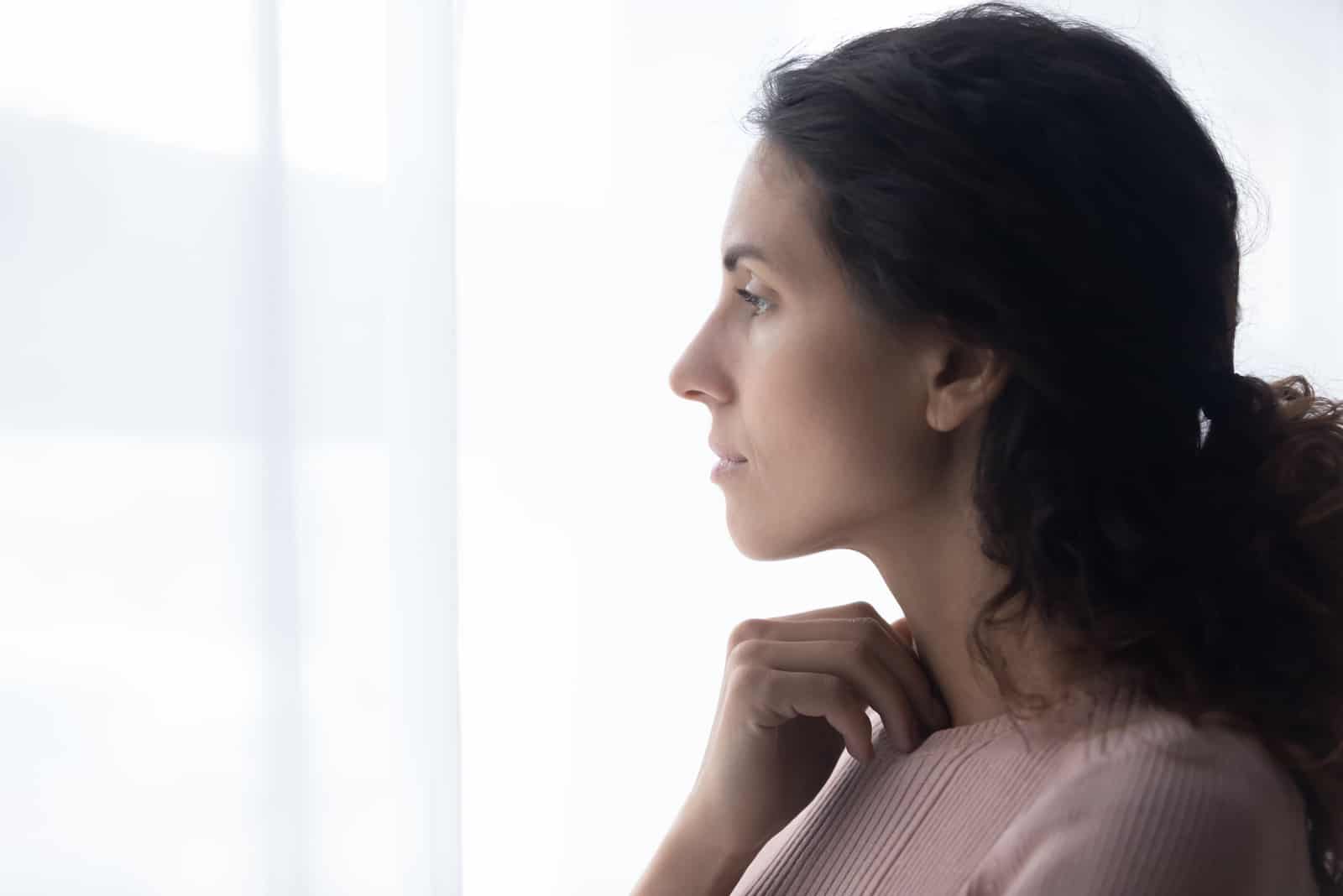 nachdenkliche junge kaukasische frau, die nahe fenster steht