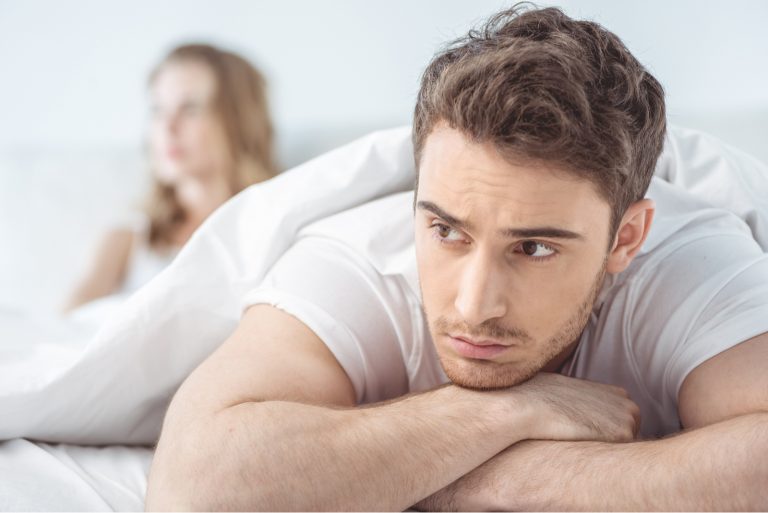 junger unzufriedener mann, der mit freundin dahinter im bett liegt