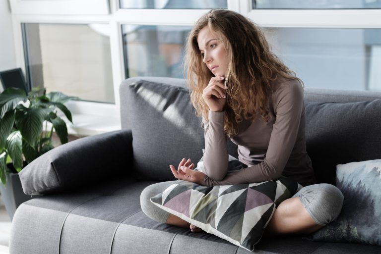 traurige junge Frau, die tief in Gedanken auf der Couch sitzt