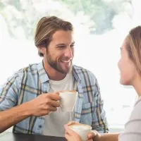 ein lächelnder Mann sitzt mit einer Frau und trinkt Kaffee