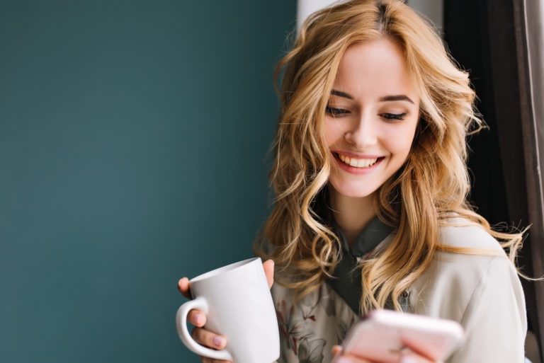 schöne blonde Frau mit Kaffeeknopf am Telefon