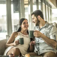 ein lächelnder Mann und eine Frau, die in einem Café auf der Couch sitzen und Kaffee trinken und reden
