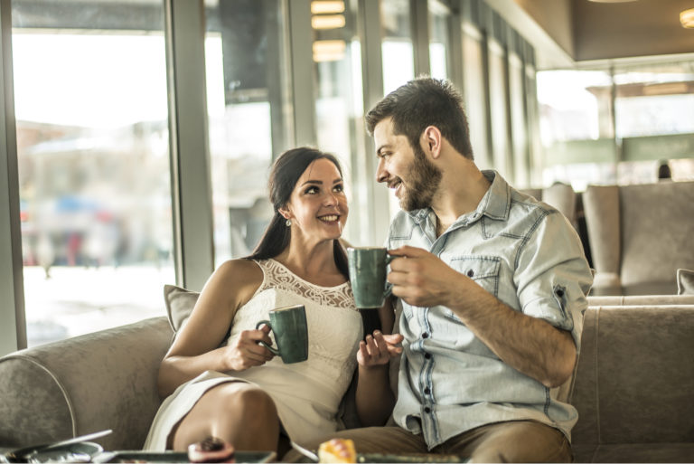 ein lächelnder Mann und eine Frau, die in einem Café auf der Couch sitzen und Kaffee trinken und reden