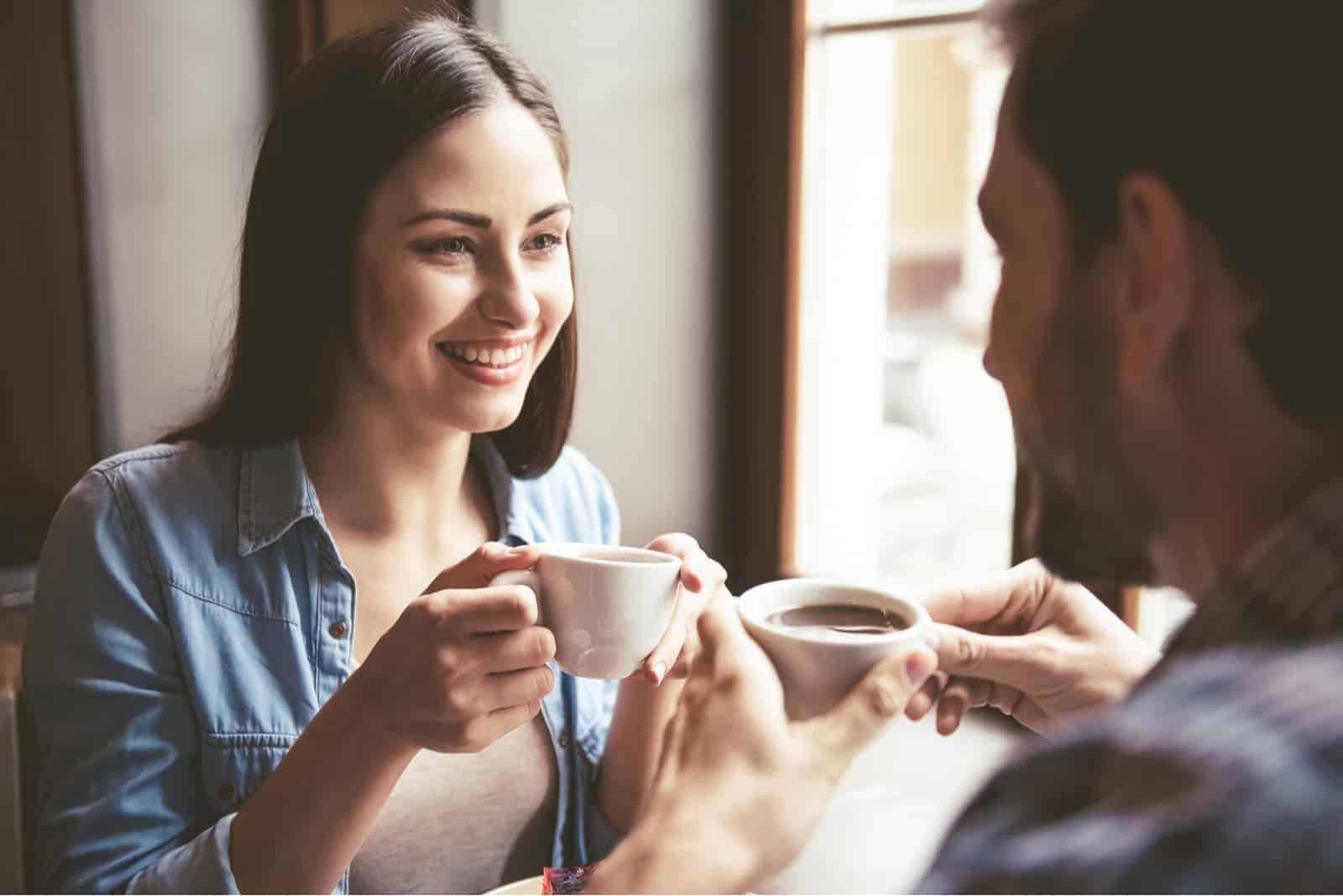 eine lächelnde Frau, die Kaffee trinkt und mit einem Mann spricht
