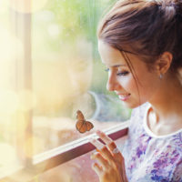 Eine schöne Frau sitzt am Fenster und spielt mit einem Schmetterling