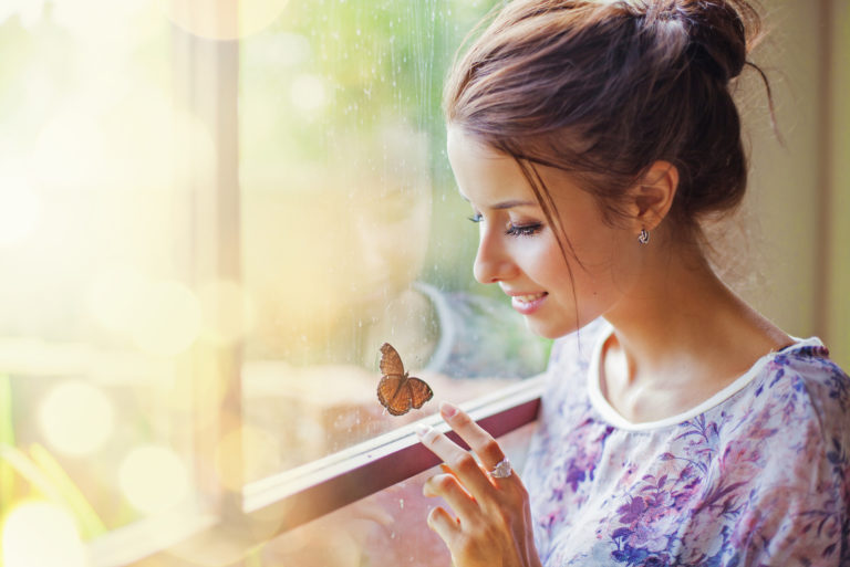 Eine schöne Frau sitzt am Fenster und spielt mit einem Schmetterling
