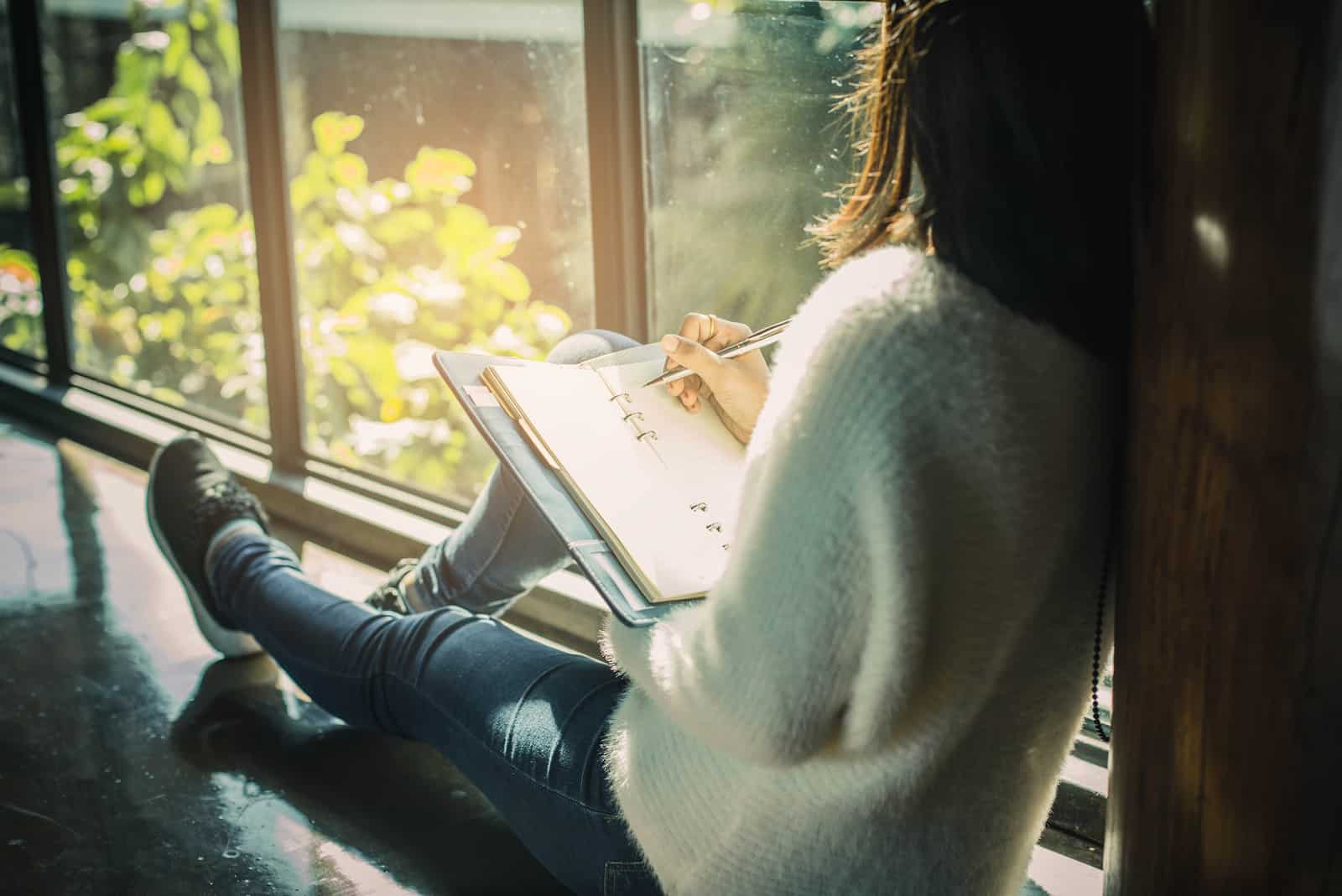 Eine Frau sitzt am Fenster und schreibt