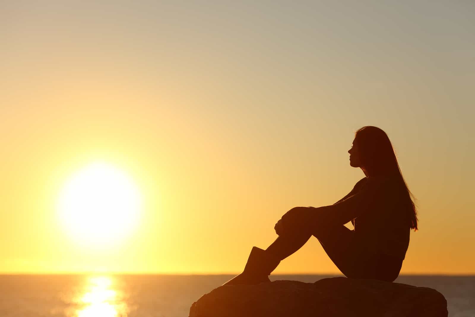 Eine imaginäre Frau sitzt und beobachtet den Sonnenuntergang