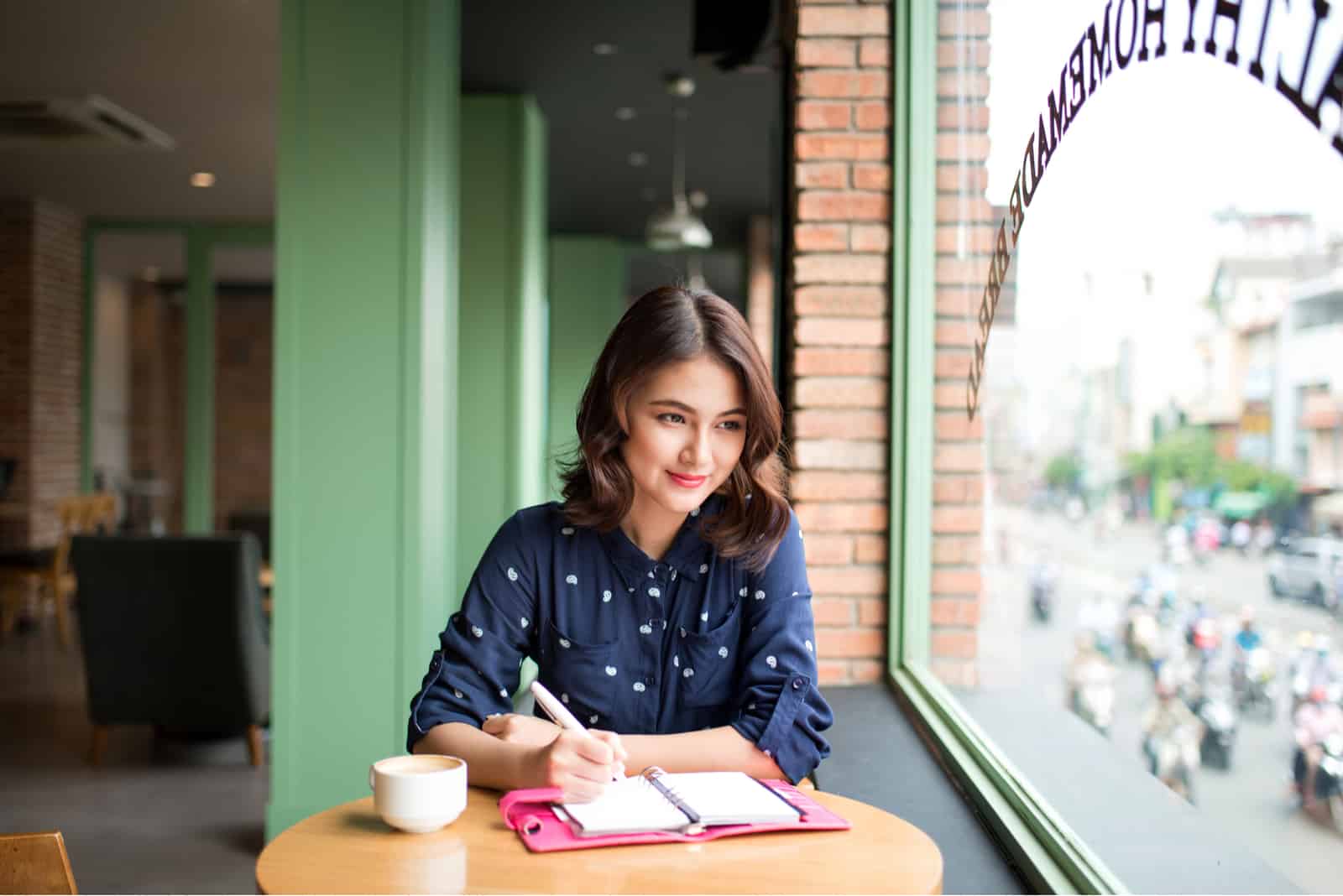 Eine schöne Frau sitzt an einem Tisch in einem Café und schreibt