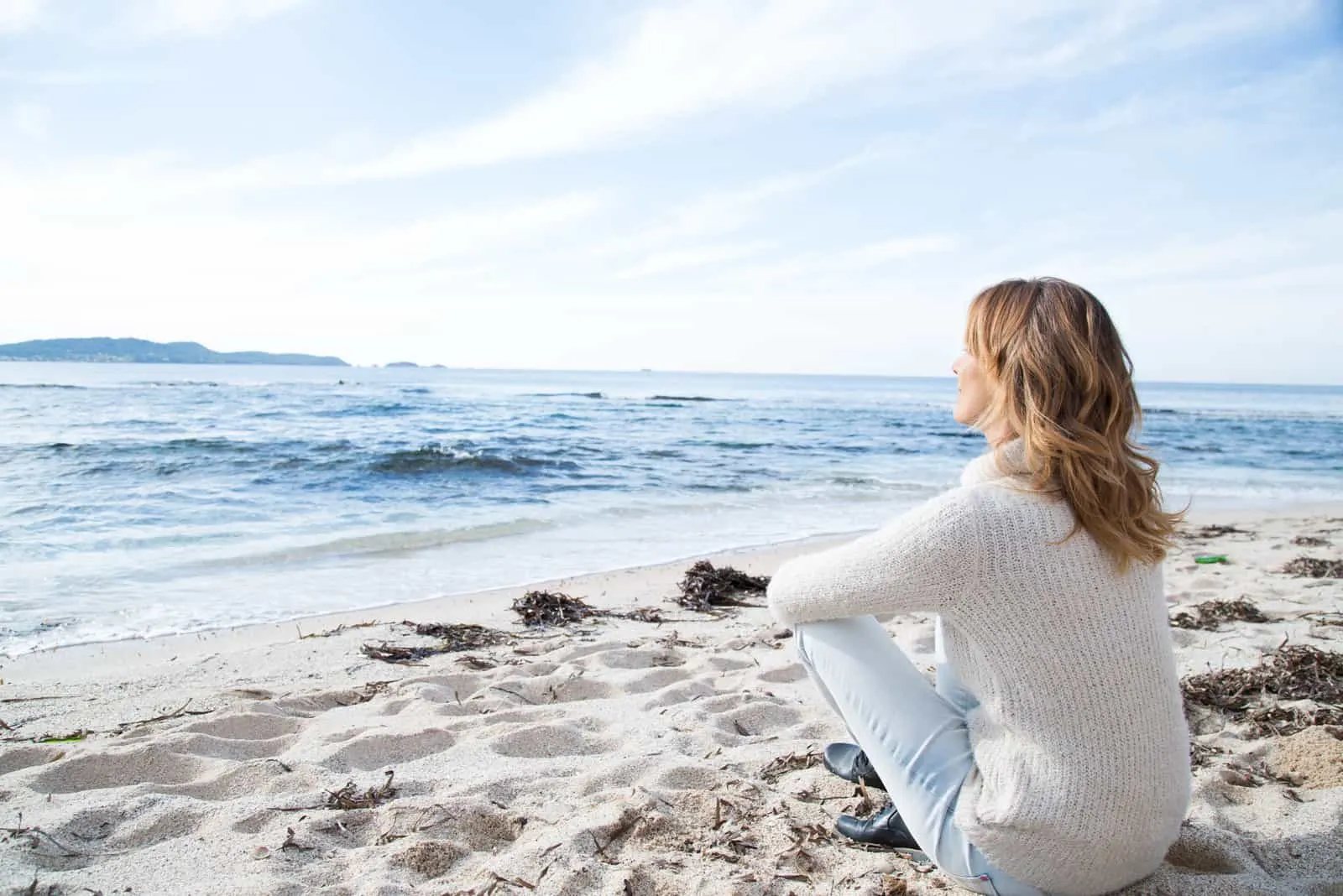 Frau sitzt allein auf dem Strand und schaut aufs Meer