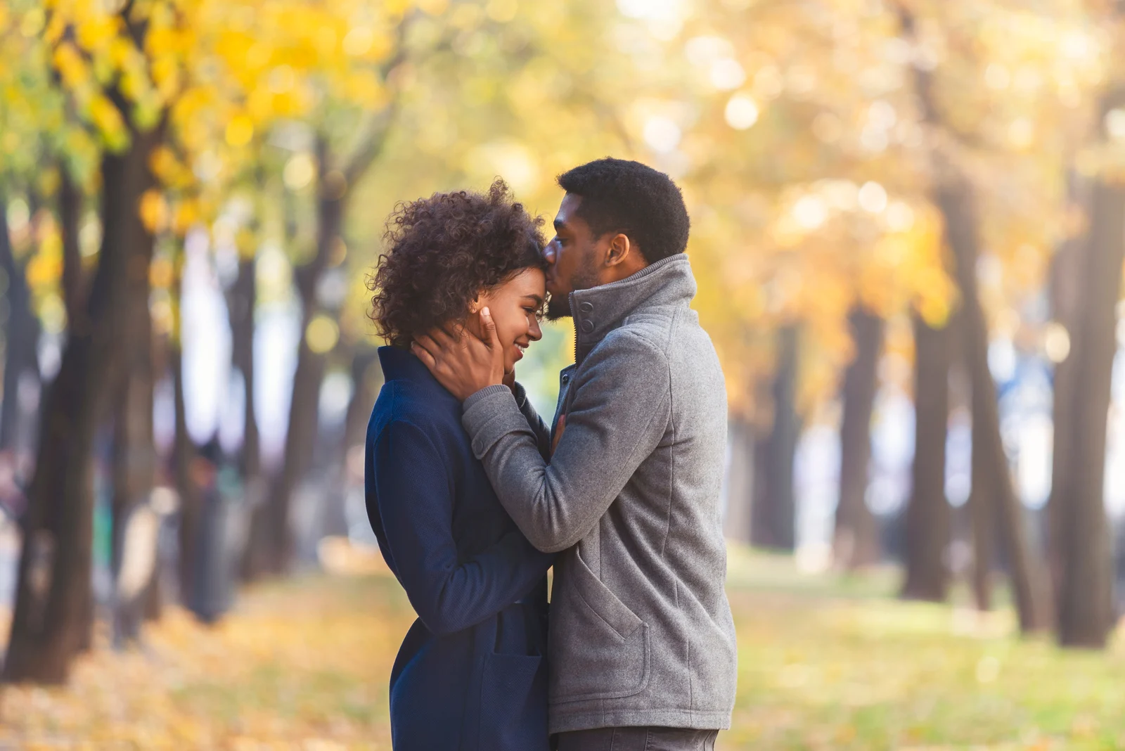 Mann küsst Frau im Park auf die Stirn