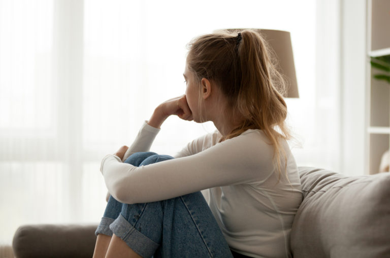 traurige Frau, die auf dem Sofa sitzt und wegschaut
