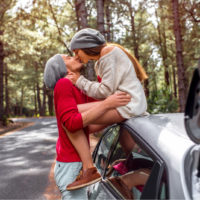 Junges und hübsches Paar, das sich in der Nähe des Autos küsst