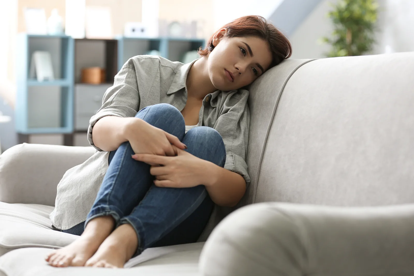 Depressive junge Frau sitzt zu Hause auf dem Sofa