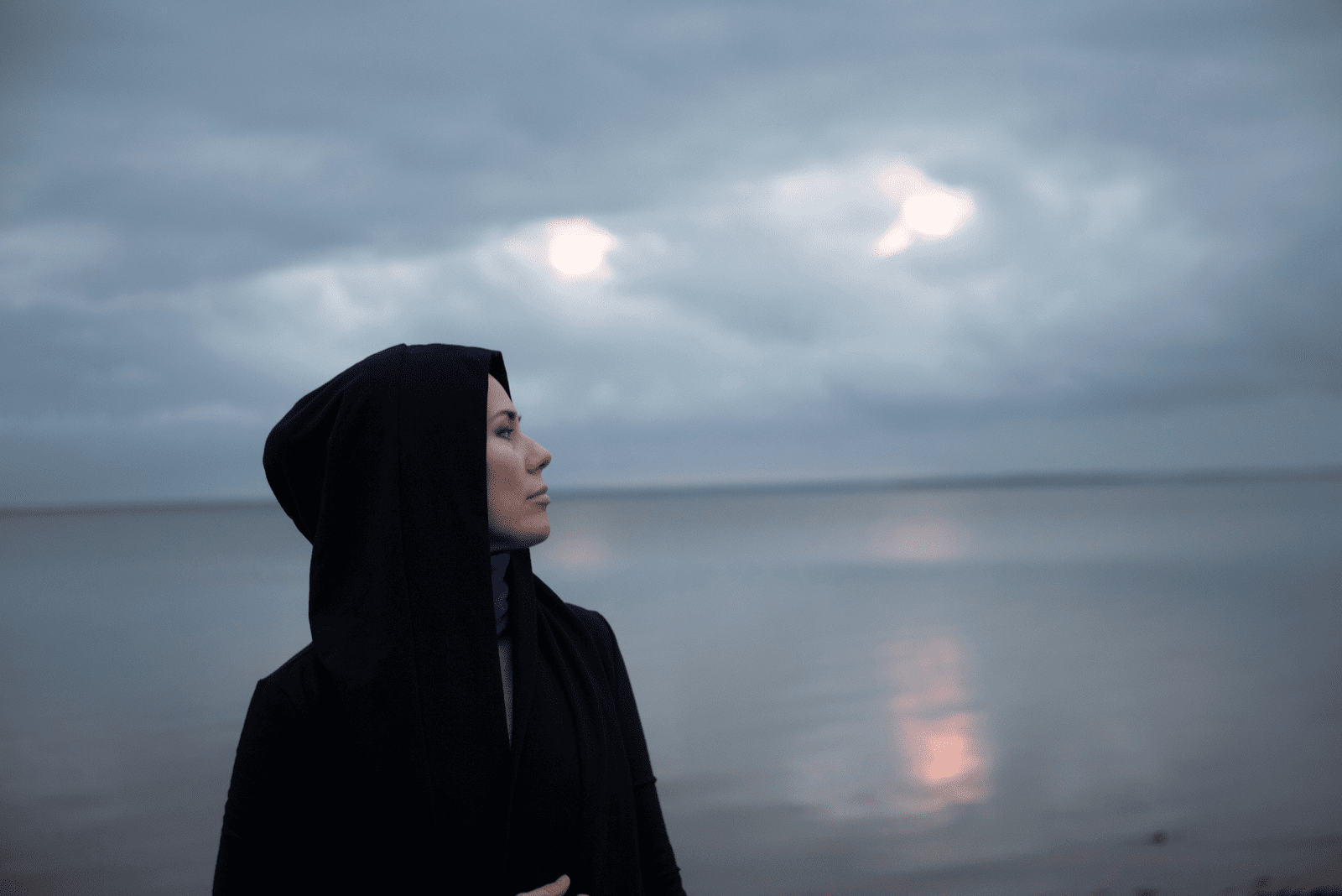Frau im schwarzen Hoodie, der am Meer steht