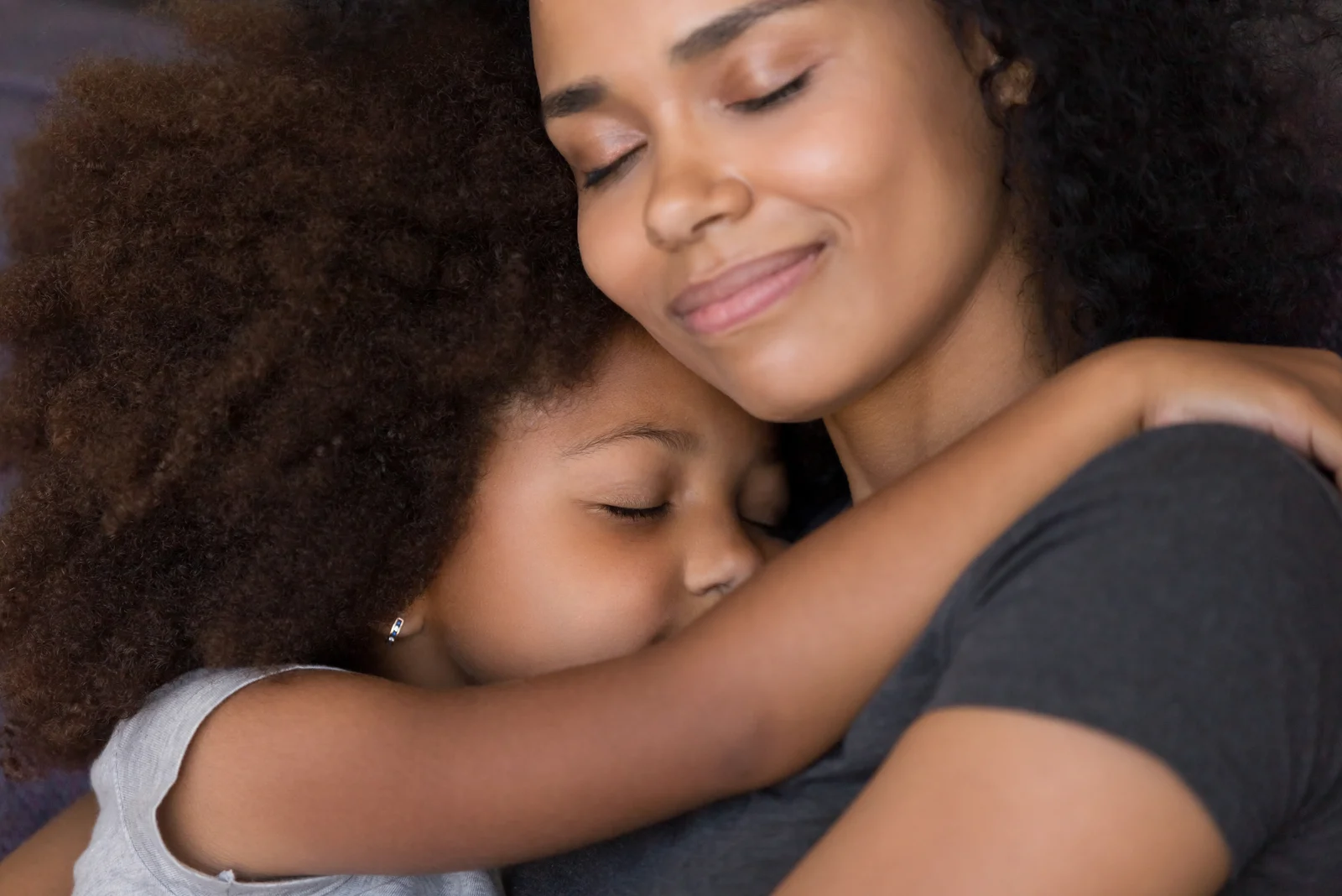 Liebevolle alleinerziehende schwarze Mutter umarmt süße Tochter