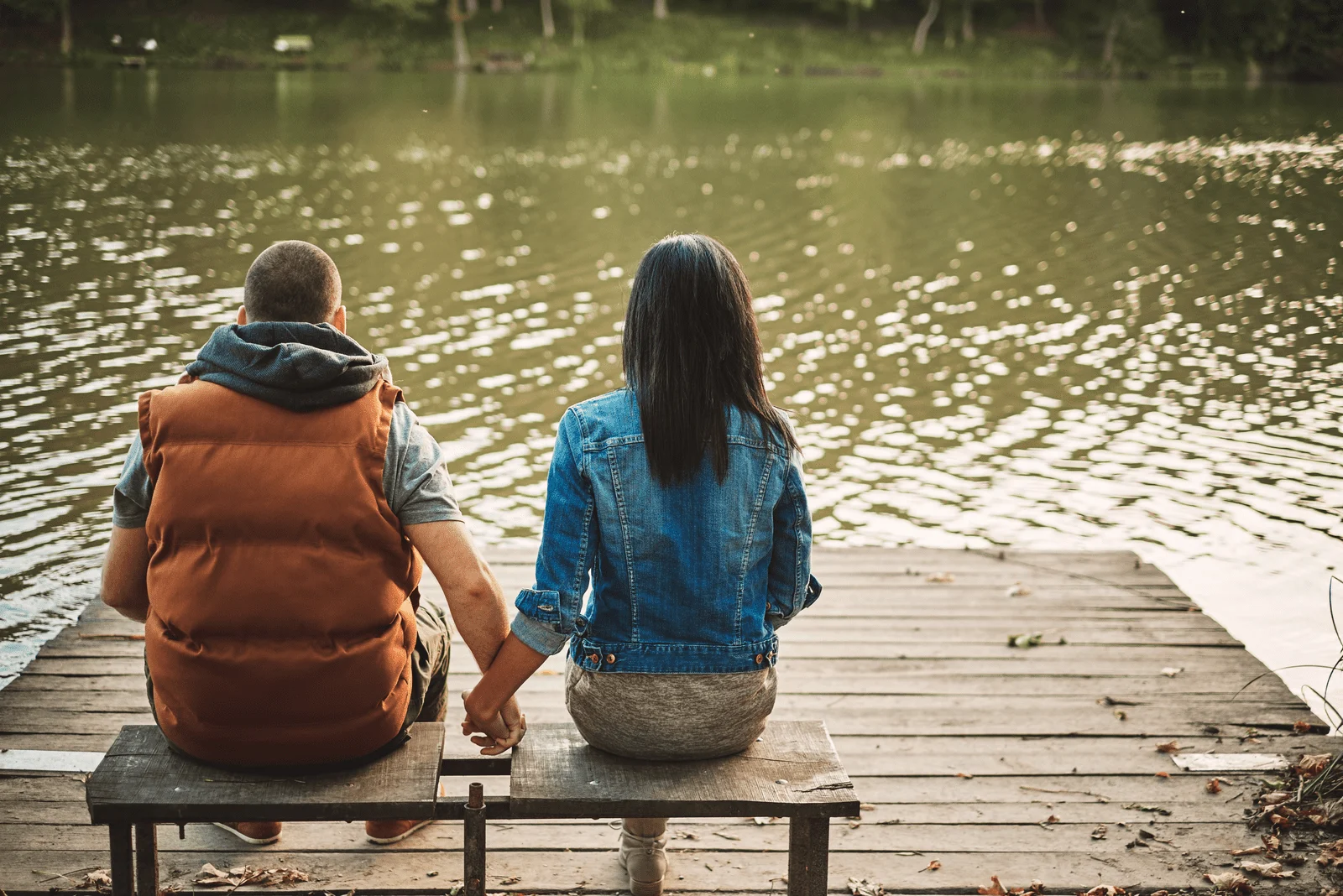 Paar sitzt auf der Bank am See und hält sich an den Händen