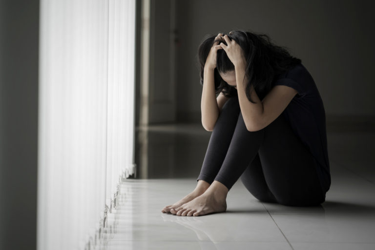 depressive Frau, die auf dem Boden sitzt und sich den Kopf hält