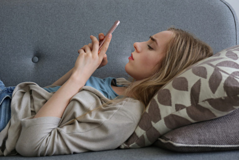 Besorgte Frau, die Smartphone hält, während sie auf der Couch liegt