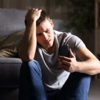 Trauriger junger Mann mit Handy auf dem Boden