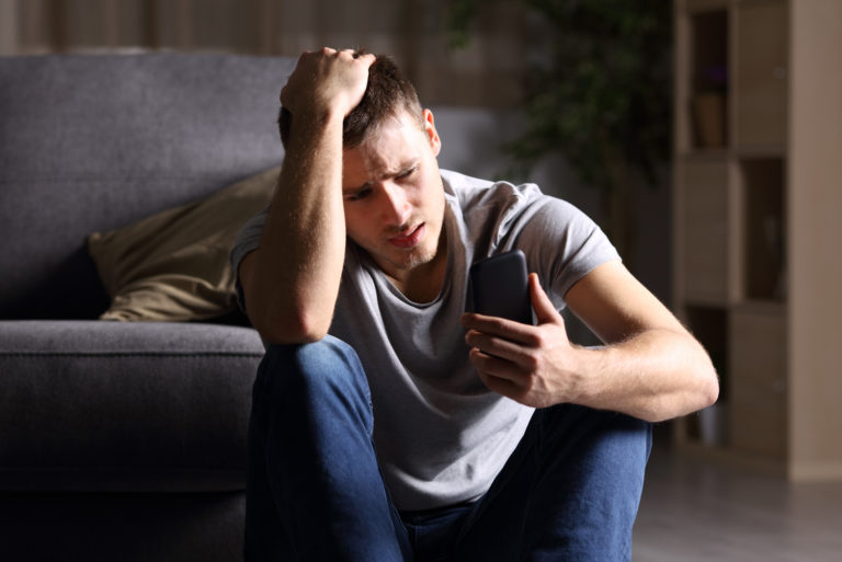 Trauriger junger Mann mit Handy auf dem Boden