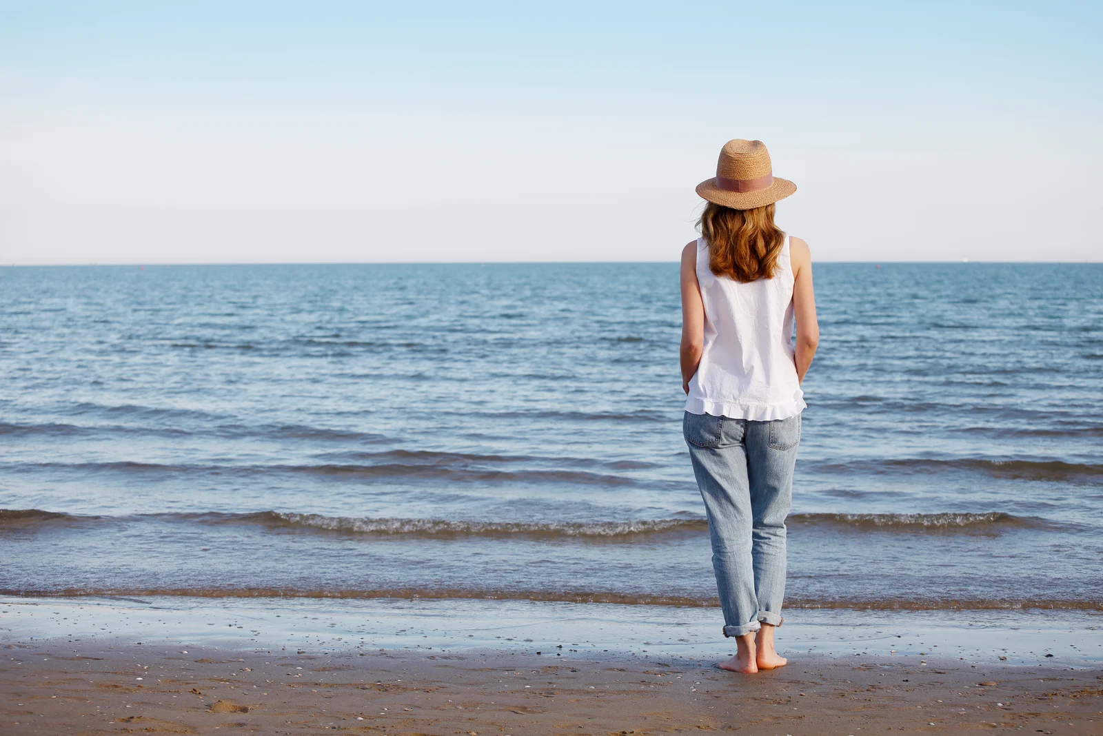 Eine Frau mit einem Hut auf dem Kopf geht am Strand spazieren