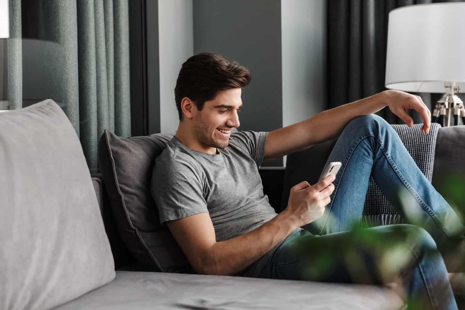 glücklicher Mann, der auf der Couch sitzt und eine SMS schreibt