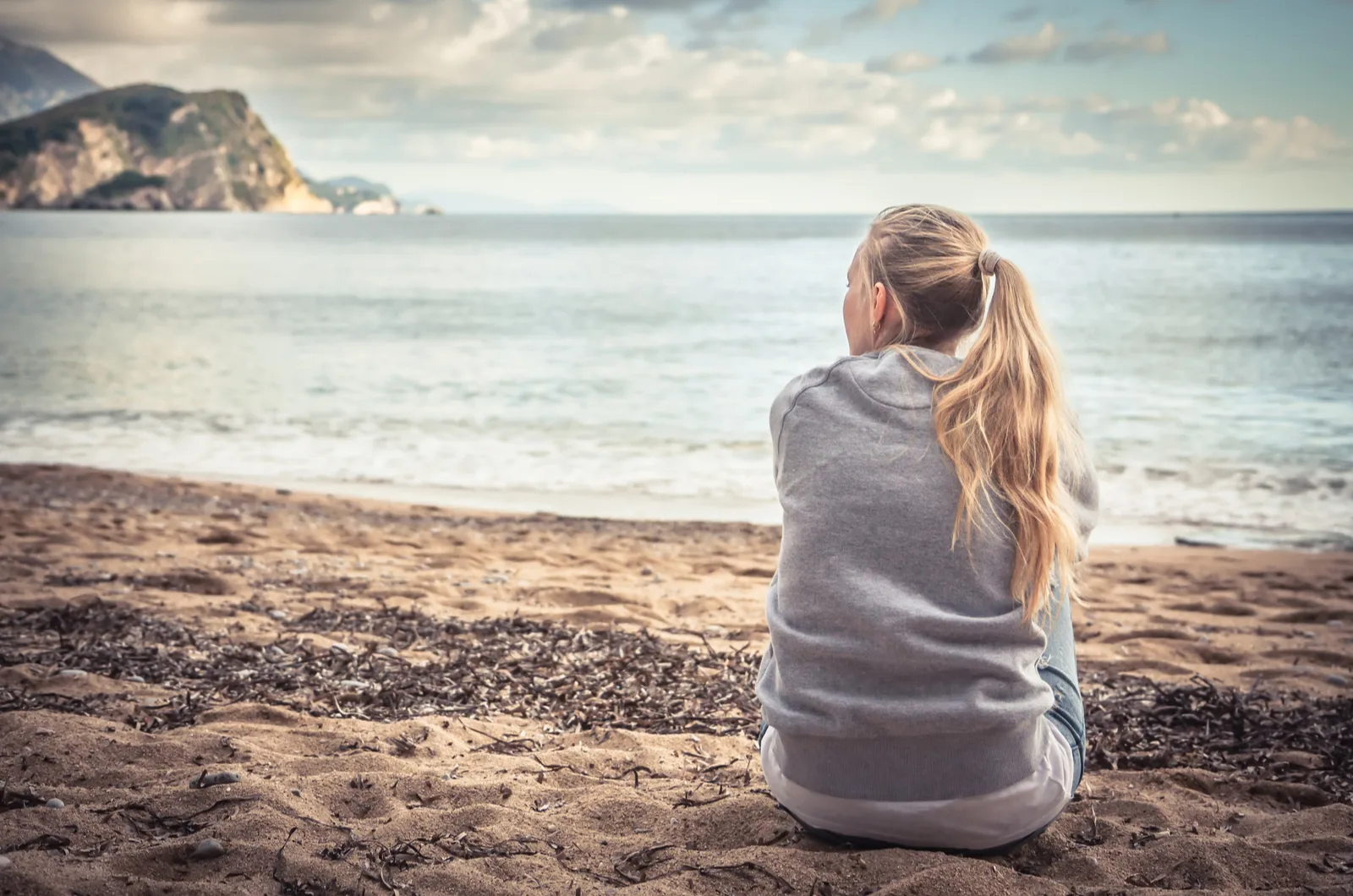 Eine Frau mit langen blonden Haaren sitzt am Strand