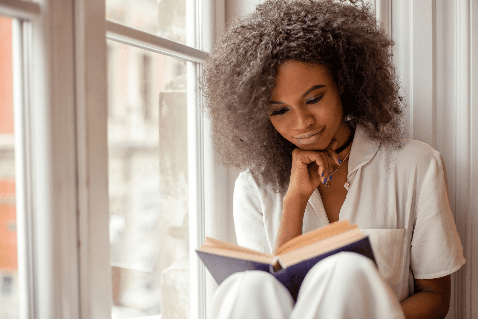 Eine Frau sitzt am Fenster und liest ein Buch