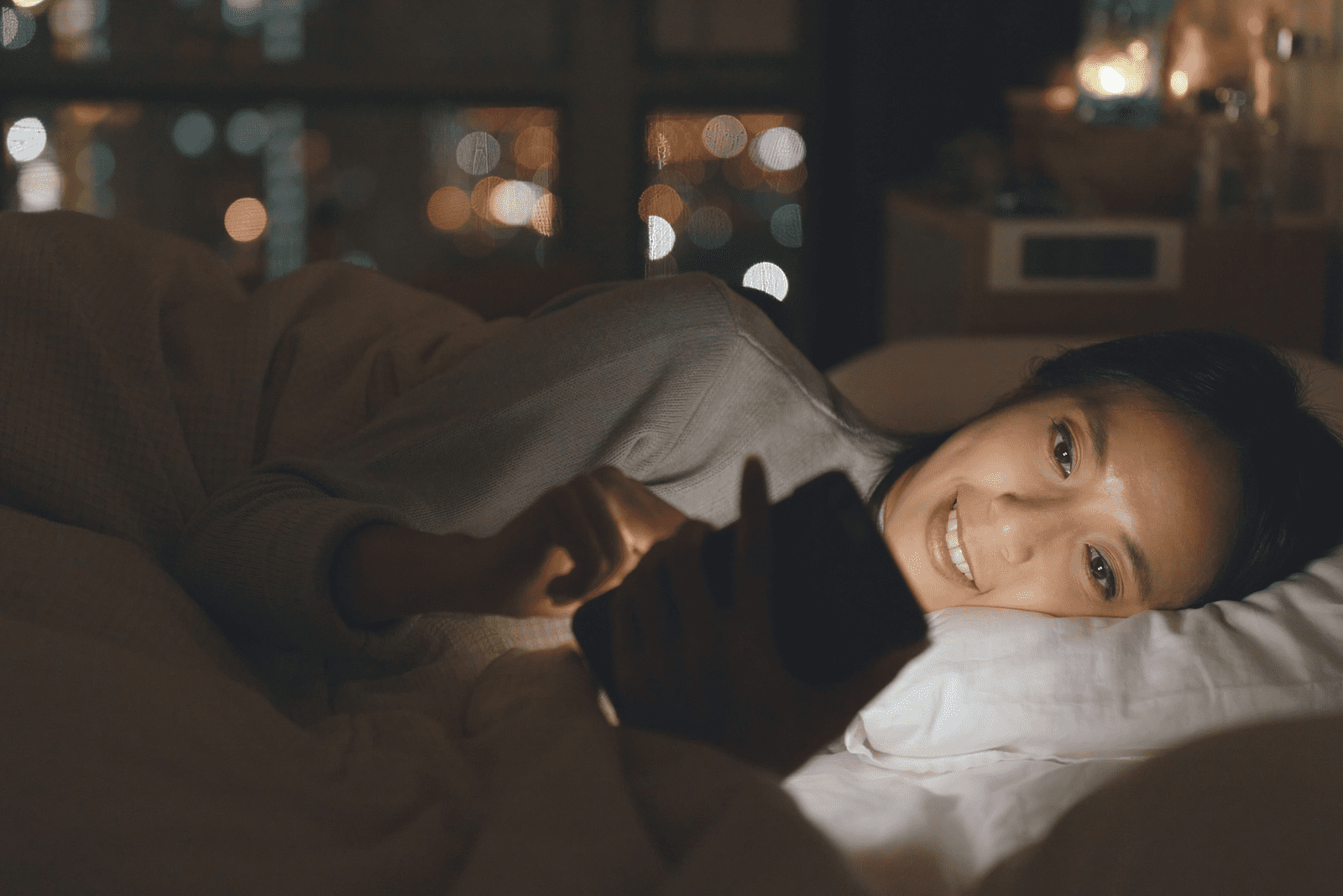 lächelnde Frau im Bett, die auf das Telefon schaut