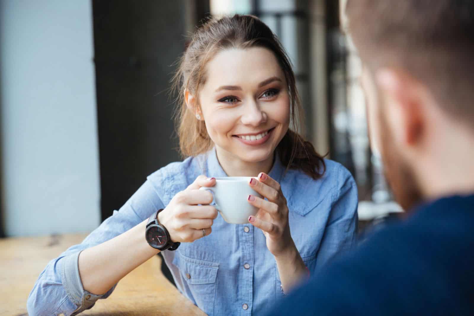 Fröhliche Frau sitzt und trinkt Kaffee im Café mit bärtigem Mann