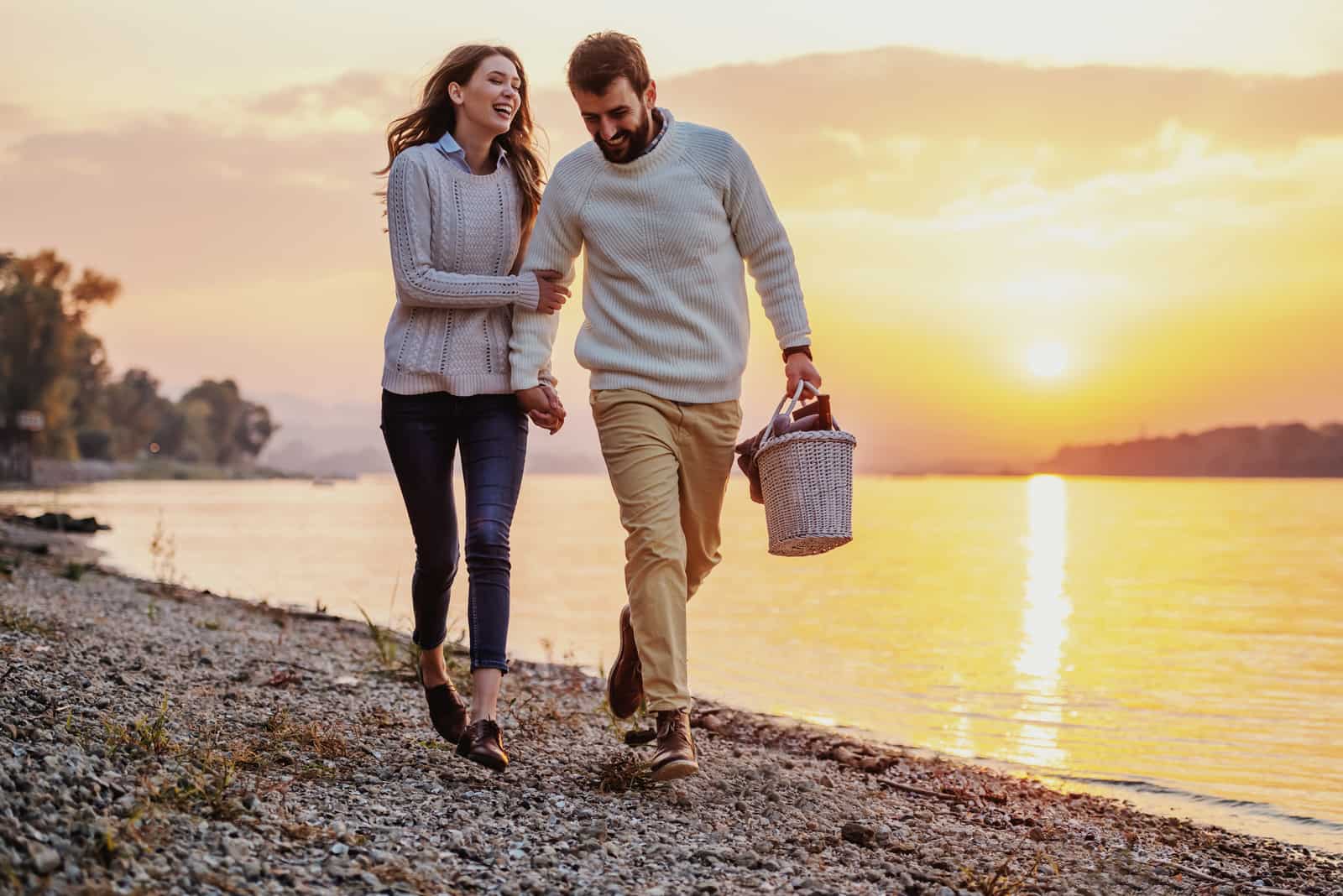 glückliches Paar, das bei Sonnenuntergang am Strand spazieren geht