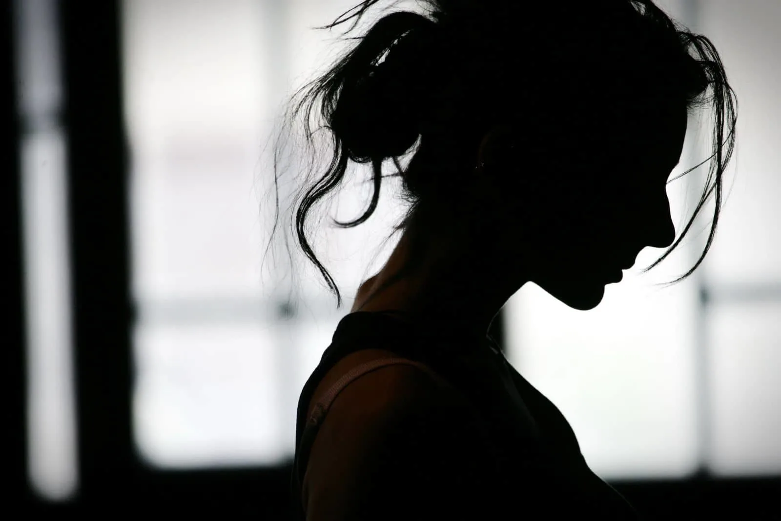Eine Frau mit zusammengebundenen Haaren steht im Dunkeln