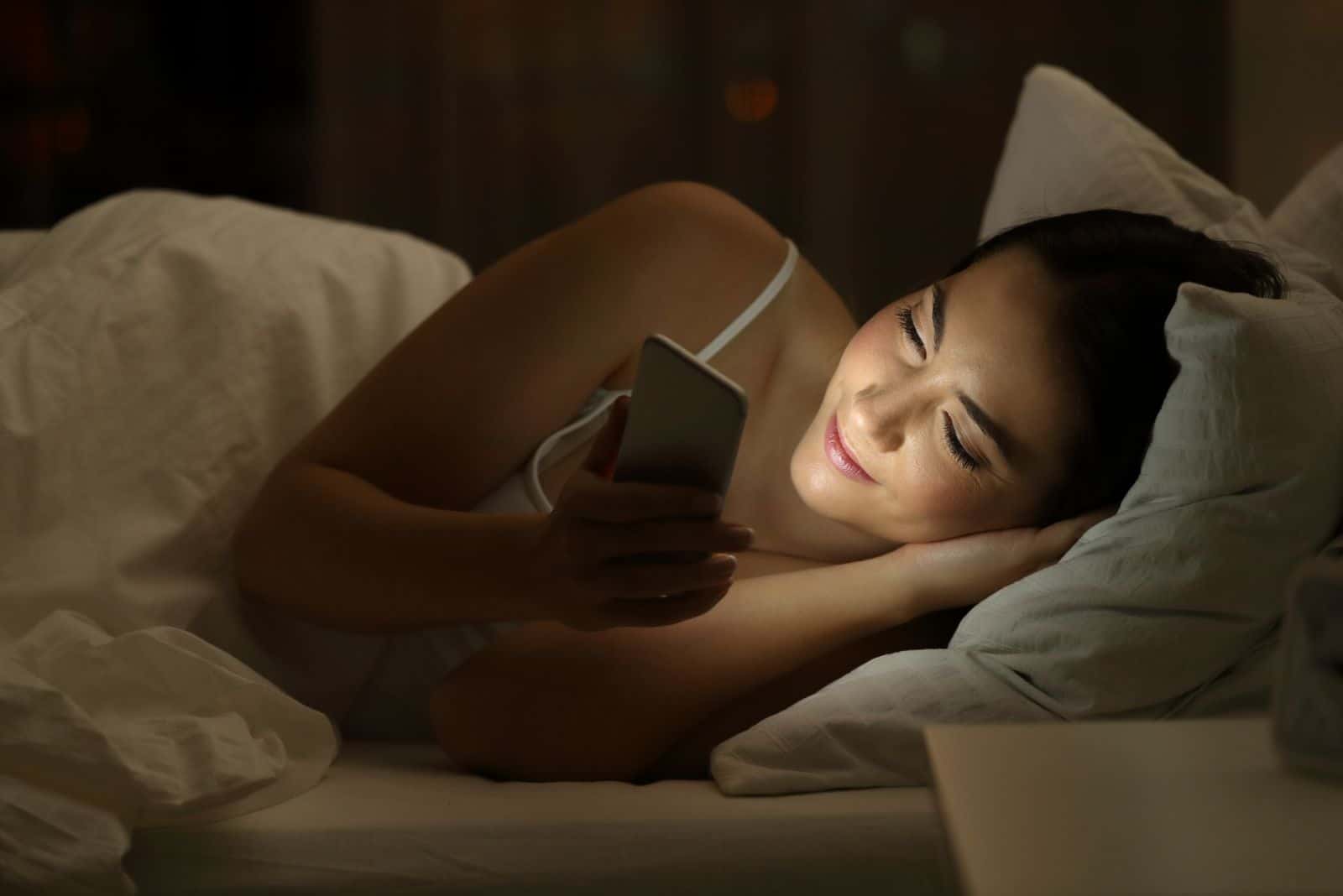lächelnde Frau im Bett mit Telefon