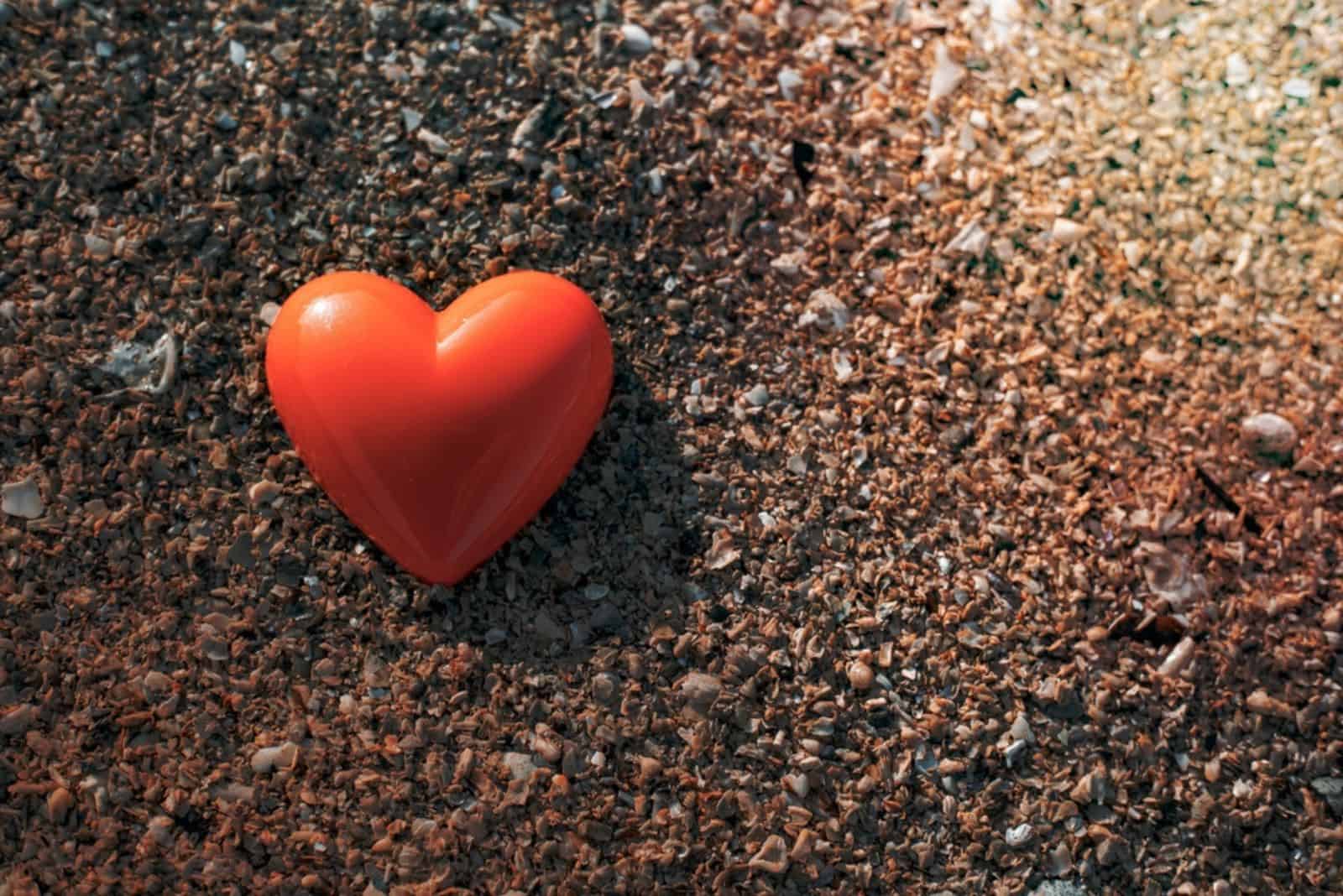 Orangefarbenes Herz am Meeresstrand und Sand